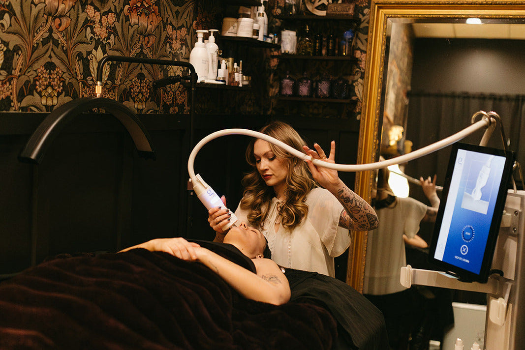 Woman receiving a facial treatment in a salon with patterned wallpaper and various products.