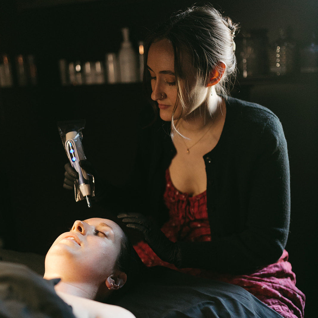Woman attending microneedling to a head with a dark background 