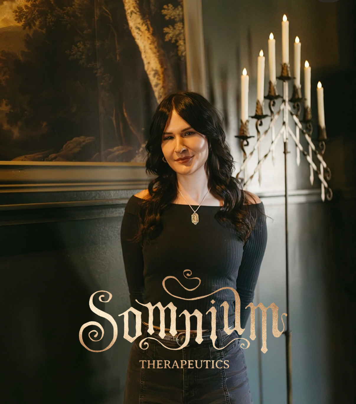 Woman standing in a room with a chandelier and painting, wearing a black top with 'Somnium Therapeutics' branding.